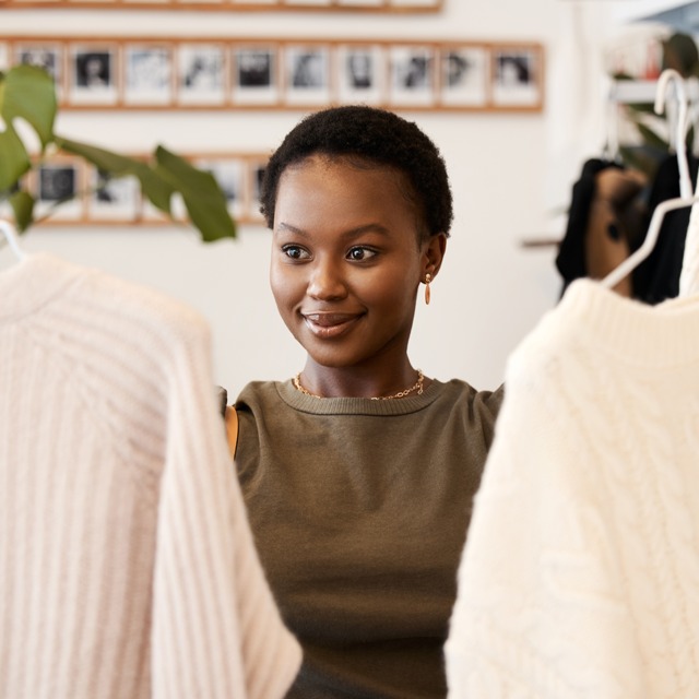 A woman choosing between two knitted sweaters at a shop